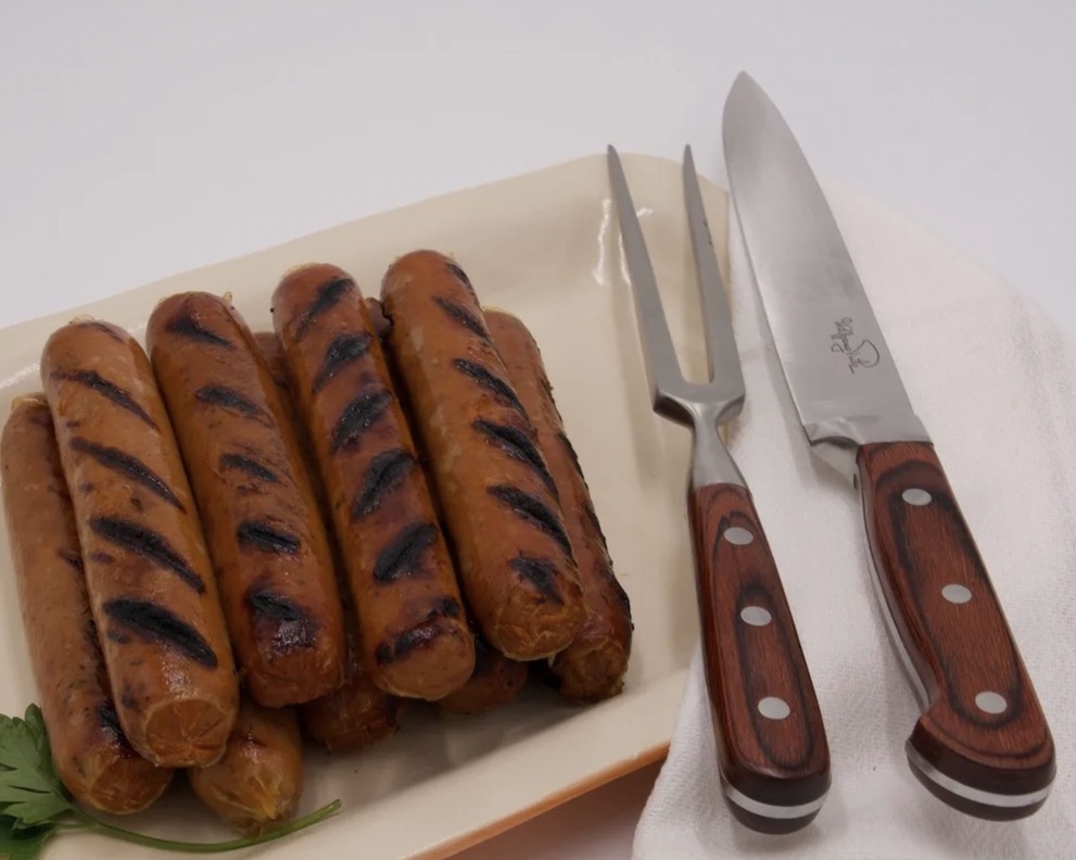 Grilled chicken sausage links on a platter with a carving knife and fork